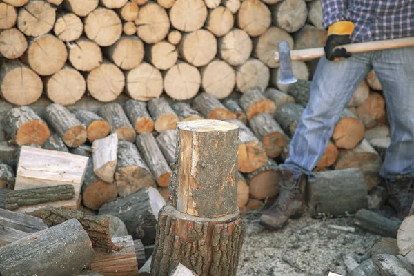 Een man met een industriële bijl. Ax in de hand. Een sterke man houdt een bijl in zijn handen tegen de achtergrond van kettingzagen en brandhout. Sterke houthakker met een bijl in zijn hand. Kettingzaag van dichtbij. — Stockfoto