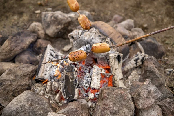 Cook sausages on a fire.
