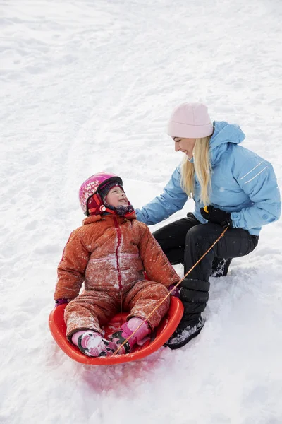 Moeder en dochter rijden op een slee vanaf een dia sneeuw. Rijden vanaf een heuvel van de sneeuw op een slee. Familie slee rijdt, slee rijdt, Winterpret, sneeuw. — Stockfoto