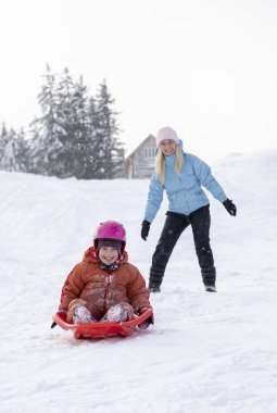 Anne ve kızı bir kar slayttan bir kızağa binmek. Bir kar tepeden bir kızağa binmek. Atlı kızak sürmek, kış eğlenceli, kar, Aile atlı kızak sürmek.