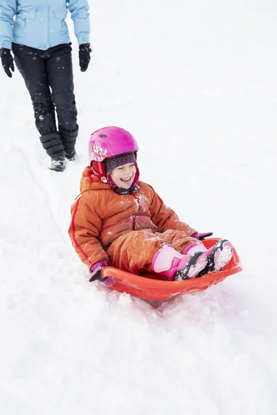 妈妈和女儿骑在雪橇上从雪地上 骑雪橇从雪山上骑下来 冬季乐趣 家庭雪橇骑行 — 图库照片