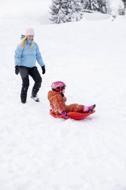 Anne ve kızı bir kar slayttan bir kızağa binmek. Bir kar tepeden bir kızağa binmek. Atlı kızak sürmek, kış eğlenceli, kar, Aile atlı kızak sürmek.