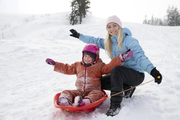 Maman et fille montent sur un traîneau d'un toboggan. Montez d'une colline de neige sur un traîneau. Randonnées en traîneau, plaisir d'hiver, neige, promenades en traîneau en famille . — Photo