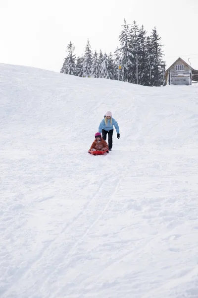 Maman et fille montent sur un traîneau d'un toboggan. Montez d'une colline de neige sur un traîneau. Randonnées en traîneau, plaisir d'hiver, neige, promenades en traîneau en famille . — Photo