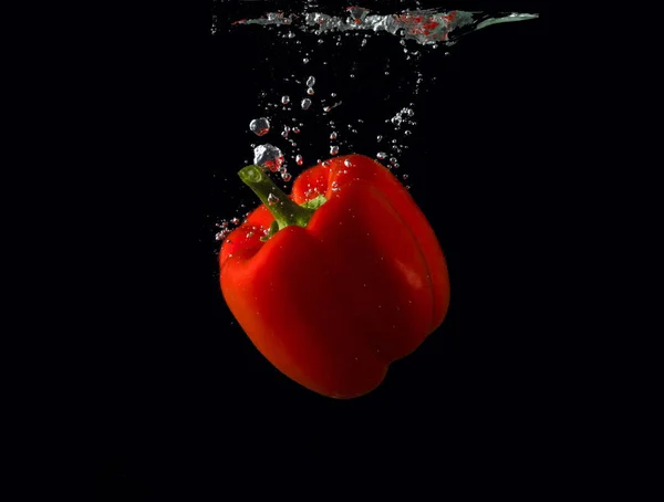 Червоний болгарський перець, що падає у воду з бризкою на чорному тлі, паприкою, стоп-фотографією. Червоний перець . — стокове фото