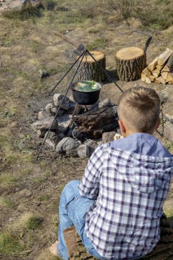 Genç çocuk yemek kazanı açık ateş üzerinde kamp yemek