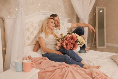 Adam yatakta güzel karısına bir çiçek ve öpücük veriyor.