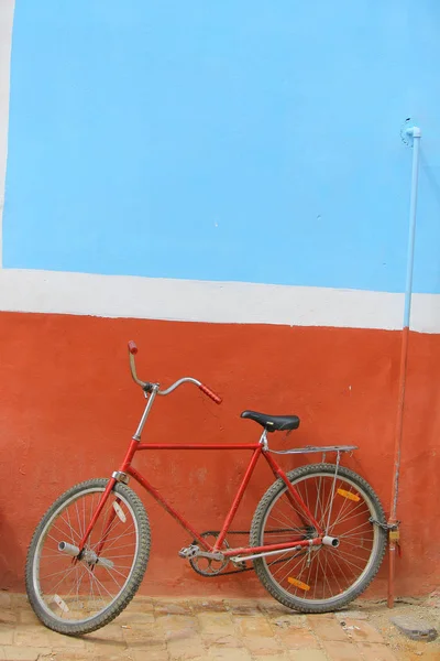 A red bike leaned toward a blue & red wall.