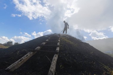  Çok az oksijen ile yavaş yanan odun yığını üzerinde iş başında bir kömür üreticisi.
