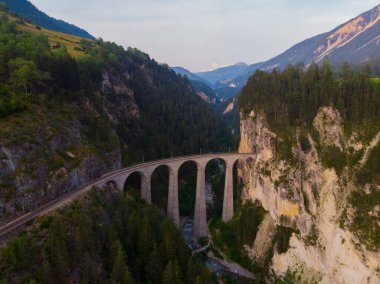 İsviçre Alpleri 'ndeki eğri bir raydaki taş bir köprüden geçen kırmızı dar gösterge..