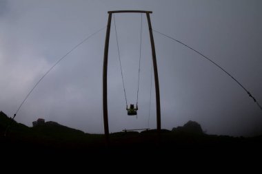 Gün batımında güzel gökyüzü ile plajda büyük salıncakta sallanan kimliği belirsiz adam. Büyük salıncak, turistlerin oynamaları için sağlanan palmiye ağacından sarkıyor..