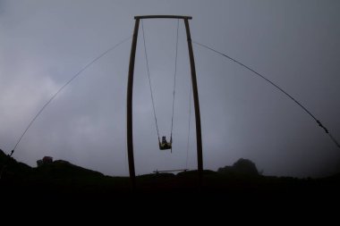 Gün batımında güzel gökyüzü ile plajda büyük salıncakta sallanan kimliği belirsiz adam. Büyük salıncak, turistlerin oynamaları için sağlanan palmiye ağacından sarkıyor..