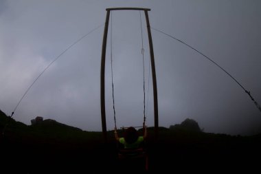 Gün batımında güzel gökyüzü ile plajda büyük salıncakta sallanan kimliği belirsiz adam. Büyük salıncak, turistlerin oynamaları için sağlanan palmiye ağacından sarkıyor..