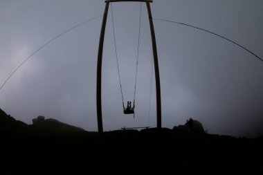 Gün batımında güzel gökyüzü ile plajda büyük salıncakta sallanan kimliği belirsiz adam. Büyük salıncak, turistlerin oynamaları için sağlanan palmiye ağacından sarkıyor..