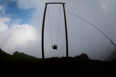 Gün batımında güzel gökyüzü ile plajda büyük salıncakta sallanan kimliği belirsiz adam. Büyük salıncak, turistlerin oynamaları için sağlanan palmiye ağacından sarkıyor..