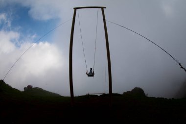 Gün batımında güzel gökyüzü ile plajda büyük salıncakta sallanan kimliği belirsiz adam. Büyük salıncak, turistlerin oynamaları için sağlanan palmiye ağacından sarkıyor..