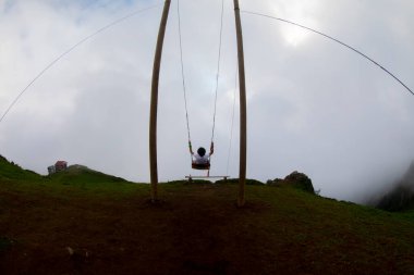 Gün batımında güzel gökyüzü ile plajda büyük salıncakta sallanan kimliği belirsiz adam. Büyük salıncak, turistlerin oynamaları için sağlanan palmiye ağacından sarkıyor..