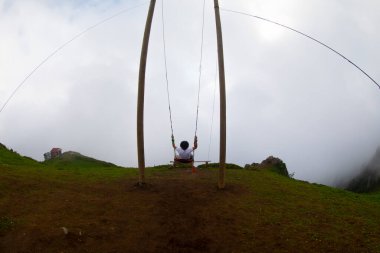 Gün batımında güzel gökyüzü ile plajda büyük salıncakta sallanan kimliği belirsiz adam. Büyük salıncak, turistlerin oynamaları için sağlanan palmiye ağacından sarkıyor..