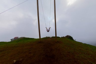 Gün batımında güzel gökyüzü ile plajda büyük salıncakta sallanan kimliği belirsiz adam. Büyük salıncak, turistlerin oynamaları için sağlanan palmiye ağacından sarkıyor..