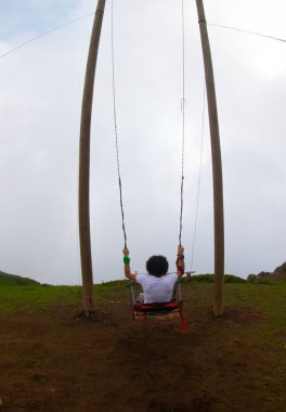 Gün batımında güzel gökyüzü ile plajda büyük salıncakta sallanan kimliği belirsiz adam. Büyük salıncak, turistlerin oynamaları için sağlanan palmiye ağacından sarkıyor..