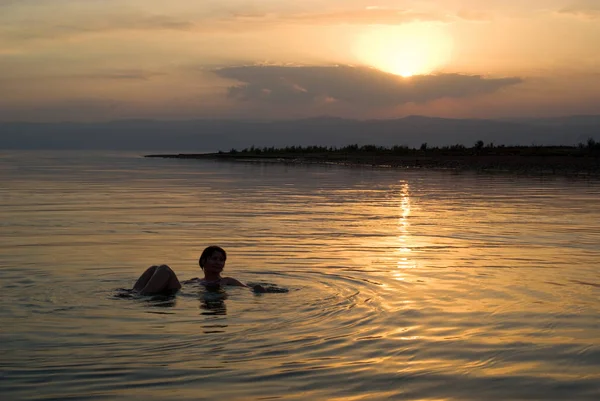 Woman floating in the Dead Sea at sunset, Jordan