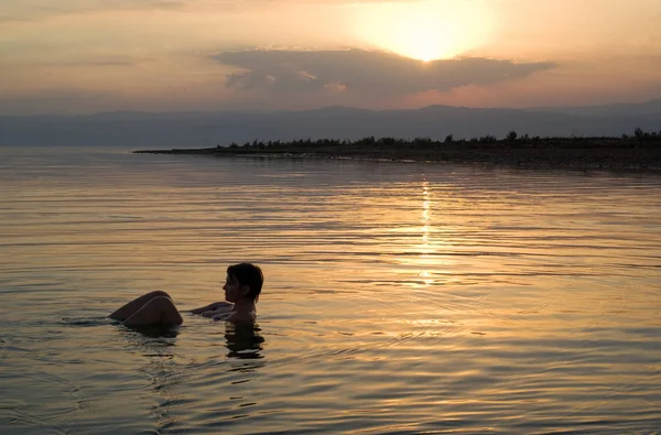 Woman floating in the Dead Sea at sunset, Jordan