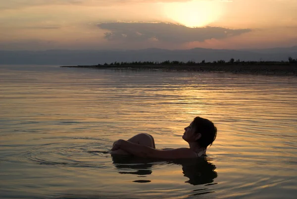 Woman floating in the Dead Sea at sunset, Jordan