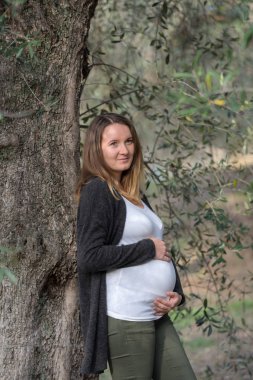 Zeytin bahçesinde duran hamile beyaz kadın.