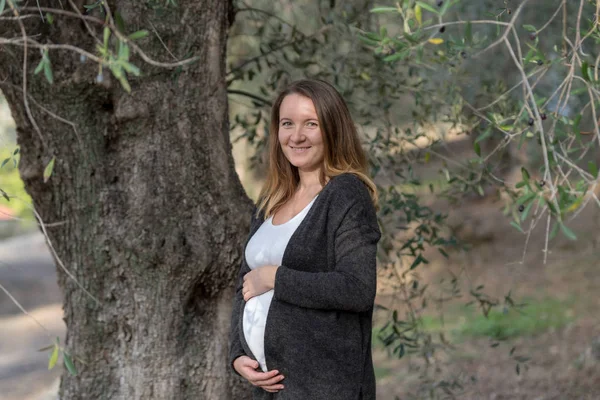 Беременная белая женщина, стоящая в оливковом саду — стоковое фото