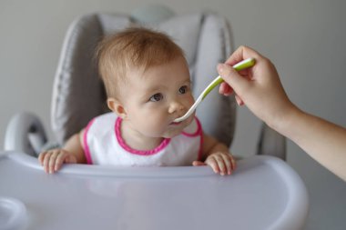 Anne, bebeğini kaşıkla yüksek sandalyede besliyor.