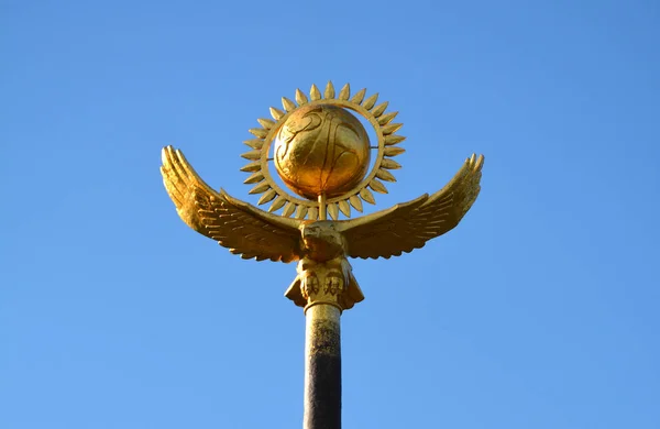 Symbols of Kazakhstan: Golden eagle and golden sun in a clean blue sky.