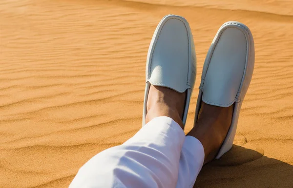 Relaxation. A gentleman\'s legs crossed in the desert sand.