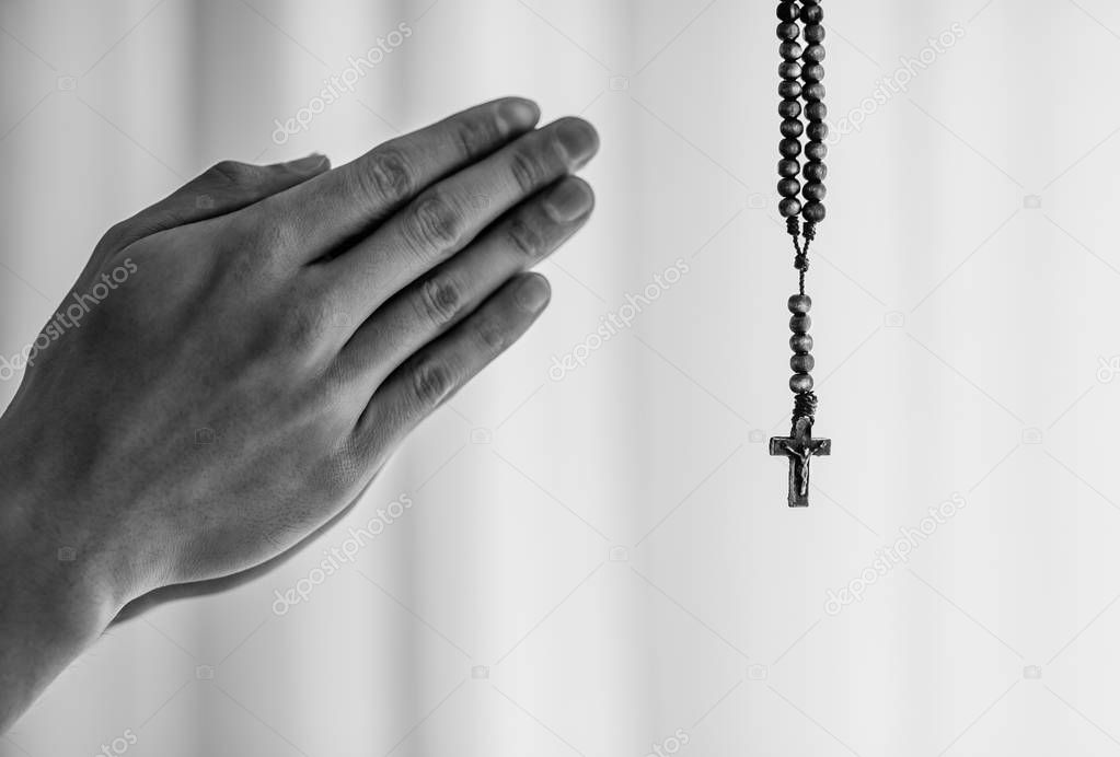 Hands together in prayer at a church and using prayer beads