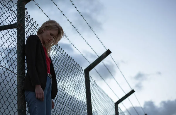 Üzgün kadın barbwire çit karşı tek başına duran.