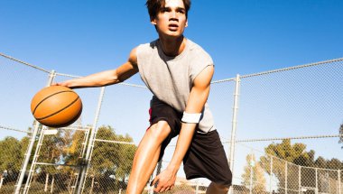 Basketbol oynayan ve dışarıda top süren genç bir erkek sporcu. Spor, motivasyon ve odaklanma.
