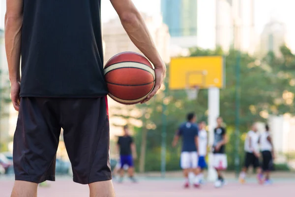 Genç basketbolcu bir yaz günü kentteki bir sahada maç izlerken elinde top tutuyor..