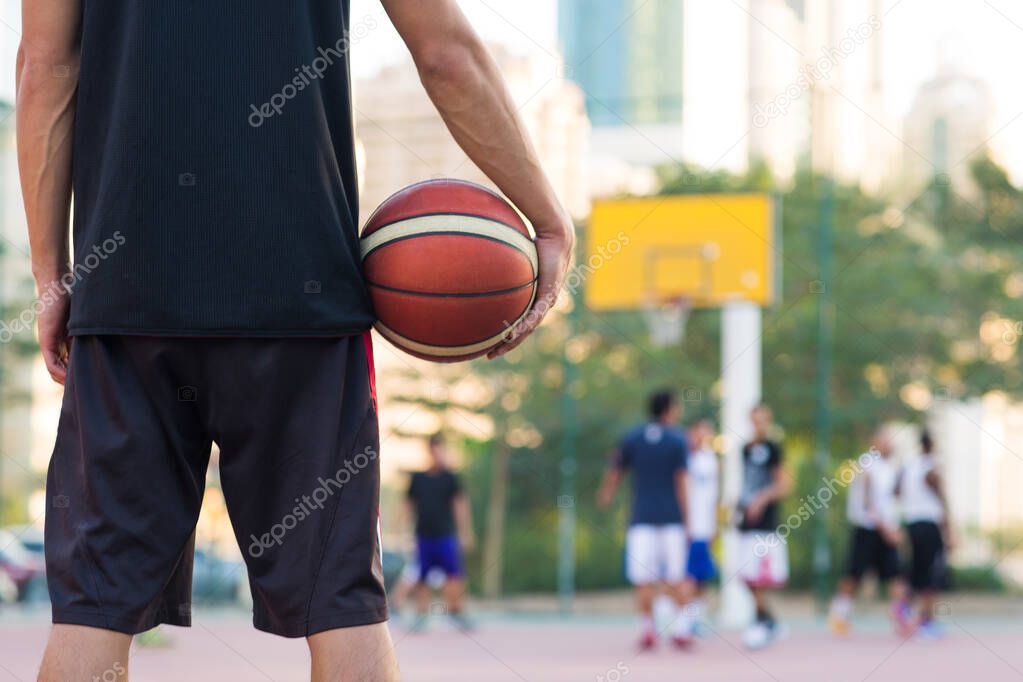 Young teen basketball player holding a ball while watching the game on an outdoor court in the city during a summer day.