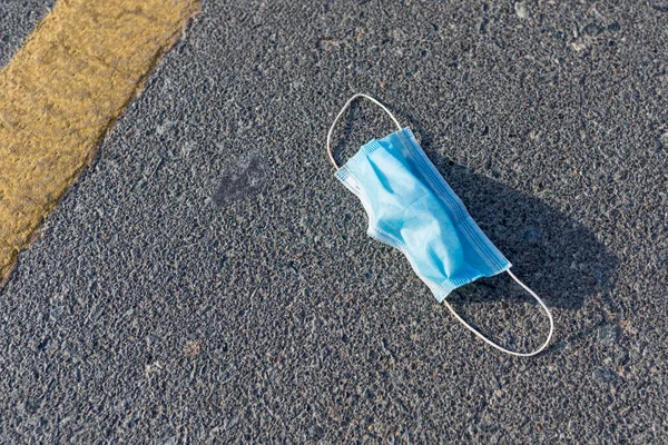 Used disposable medical face mask left discarded on the road. Environmental pollution and waste during the Covid-19 pandemic.