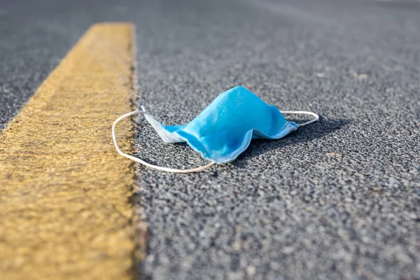 Used disposable medical face mask lying on the ground of a road. Pandemic littering and environmental pollution concept.