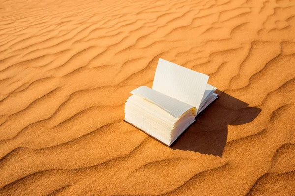 Beautiful open book with pages flipping lying in the desert sand dunes during sunset. Reading and writing in nature concept.