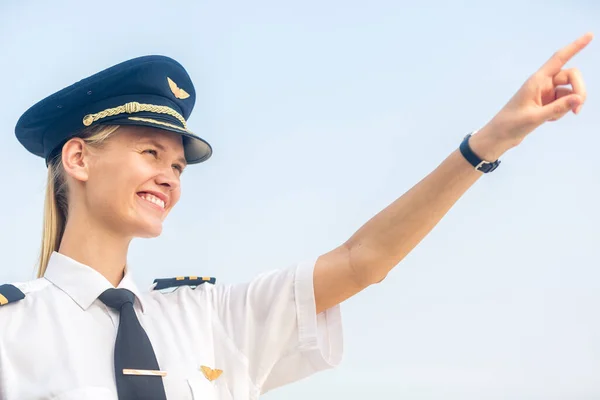 Üniformalı neşeli genç bayan pilot gökyüzüne bakıyor ve onu işaret ediyor. Ticari havayolu ve havayolları kariyeri.