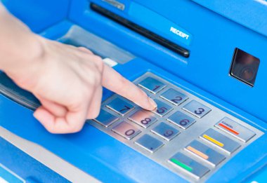 Bir erkeğin elinin mavi ATM 'deki bir ATM' nin tuş takımının şifresini girerken görüntüsü..