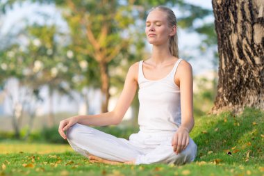 Dışarıda huzur içinde meditasyon yapan rahat genç bir kadın yaz boyunca bacak bacak bacak üstüne atmış bir şekilde parkta oturuyor. Sağlık, sağlık ve öz bakım..