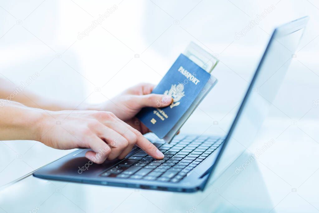 Closeup male person's hands holding a US passport with money while typing online on laptop computer keyboard. Internet travel booking.