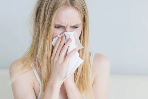 Sick young woman with a cold blowing her nose into a tissue paper at home. Close-up.