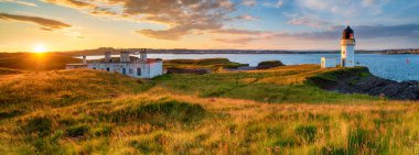 Panoramic view of sunset over the lighthouse and coastguard cottages at Arnish Point in Stornoway harbour on the Isle of Lewis in Scotland clipart