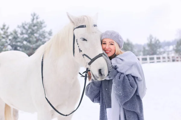 Young happy smiling attractive blond woman with horse, overcast winter day