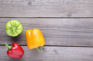 Gri bir ahşap zemin üzerinde kırmızı, yeşil ve sarı biber