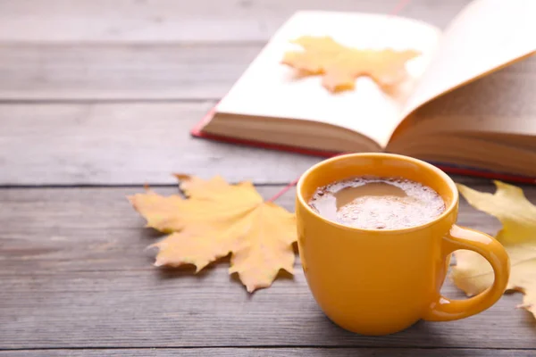 Cup of coffee with autumn leaf and book on grey background. Cozy concept