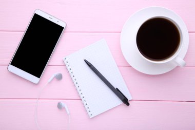 Defter ve pembe ahşap zemin üzerine kahve ile akıllı telefon